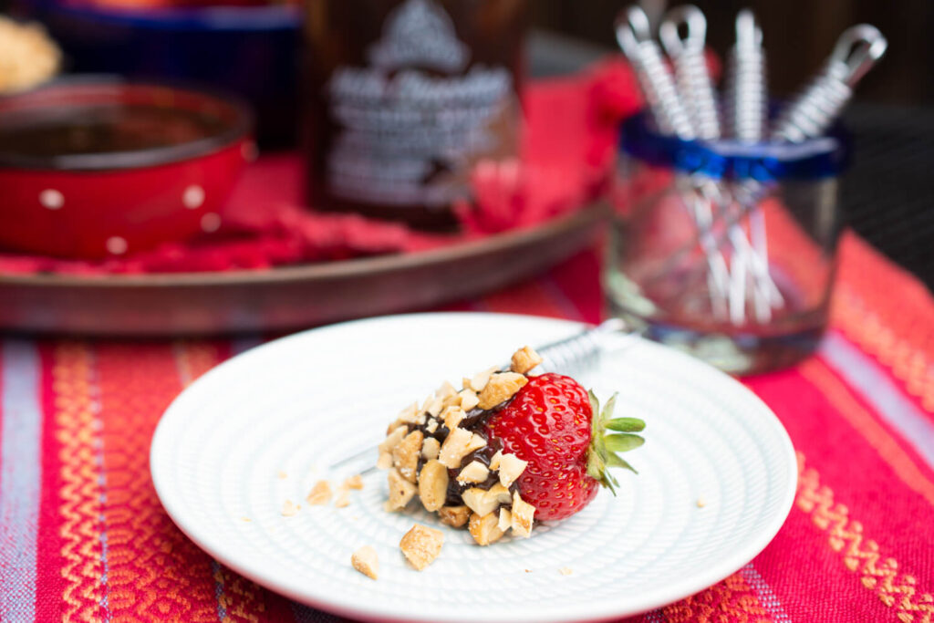 Close up image of a single chocolate-dipped strawberry covered in chopped cashews on a white plate