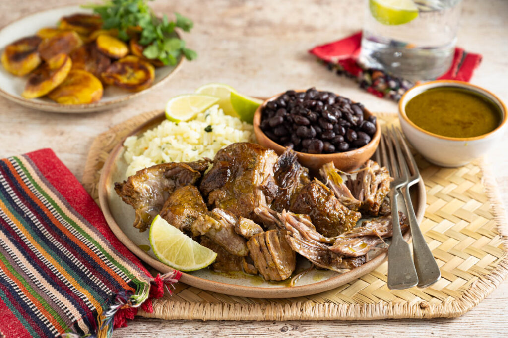Plate of pulled pork with wedge of lime and bowl of black beans