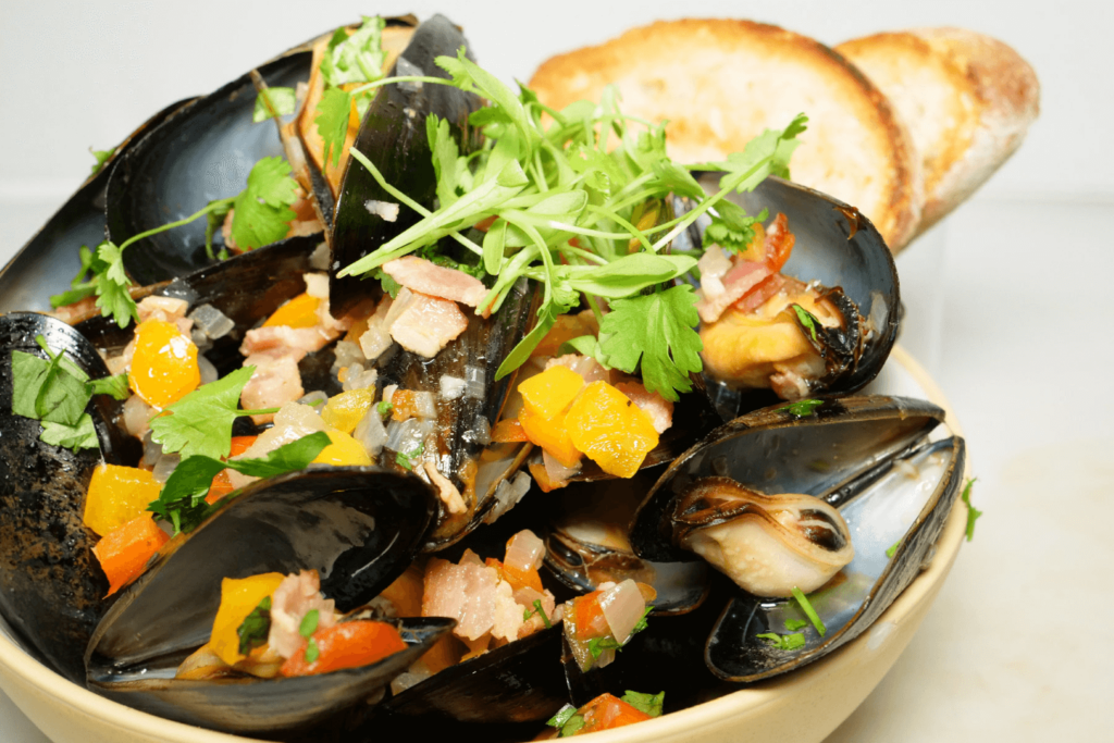 Rainbow pepper mussels in bowl garnished with curly parsley.