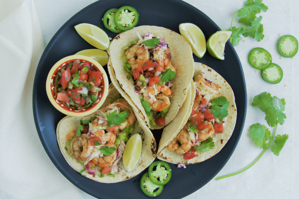 Summer Recipe: Black plate with three spicy shrimp tacos, garnished with lime and jalapenos.