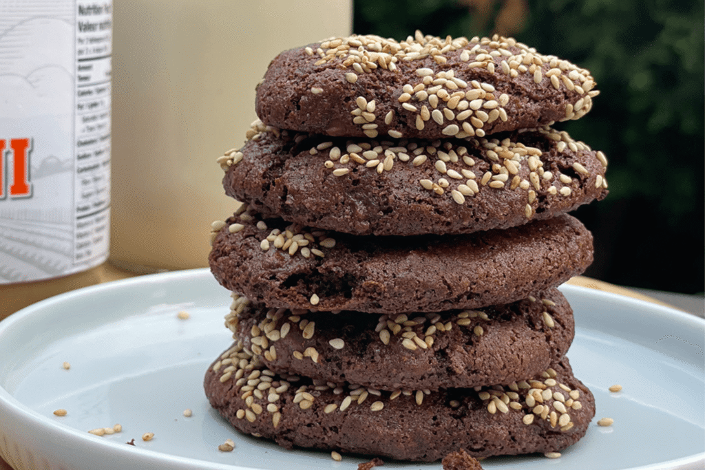 Stack of five chocolate sesame seed cookies on a white plate outdoors