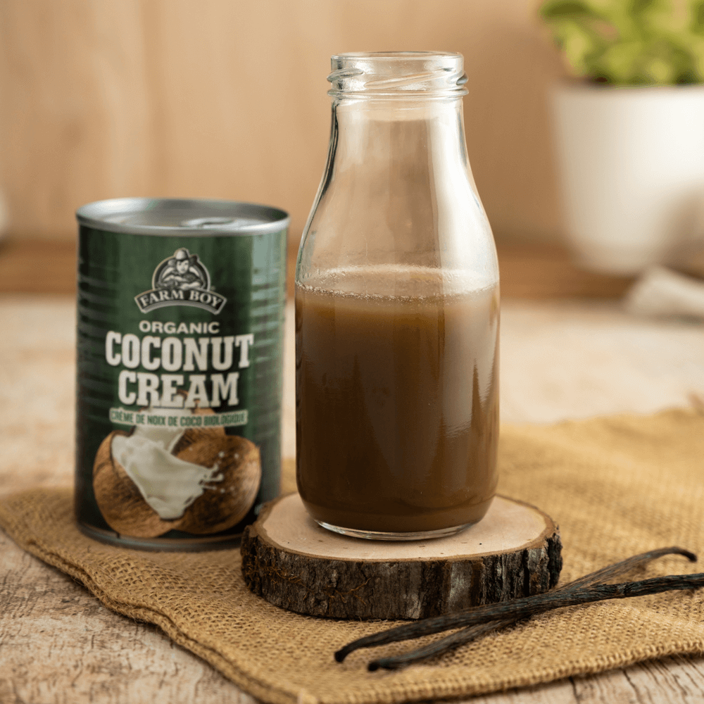 Glass bottle of coconut-infused maple syrup on a raw wood coaster next to can of Farm Boy Coconut Cream.