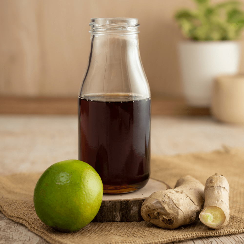 Glass bottle of maple syrup on wooden coaster with whole lime and two pieces of raw ginger root.