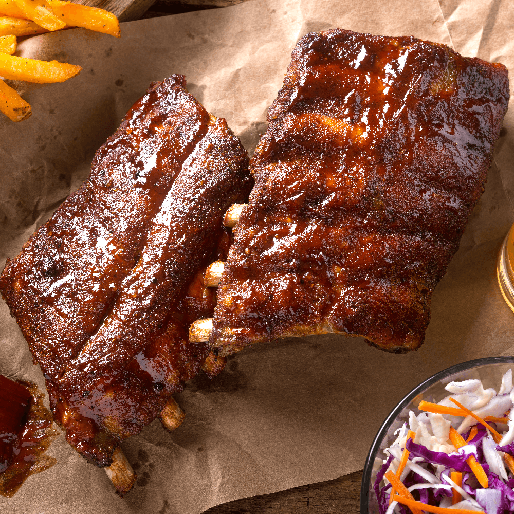 Two slabs of pork back ribs on butcher paper with coleslaw in the corner.