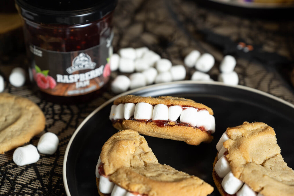 Plate with cookie sandwiches with marshmallows arranged as teeth with jar of Farm Boy Raspberry Jam in background