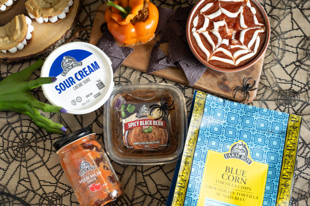 Overhead image of Halloween-inspired bean dip with cobweb drawn on it, surrounded by Farm Boy items