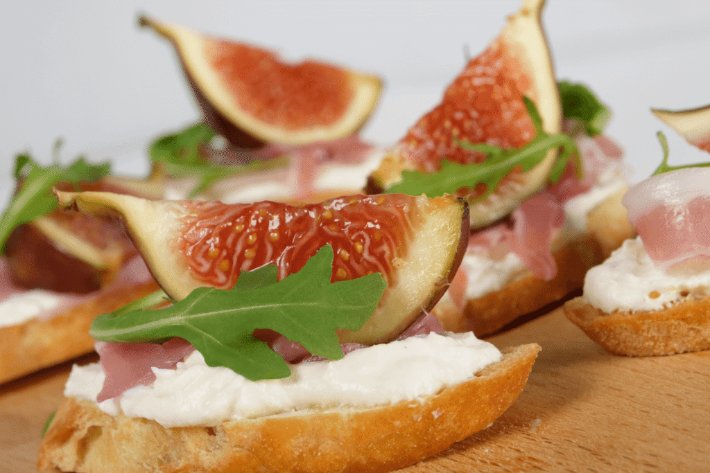 Close up of sliceds of crostini with goat cheese, prosciutto, fresh fig, and arugula