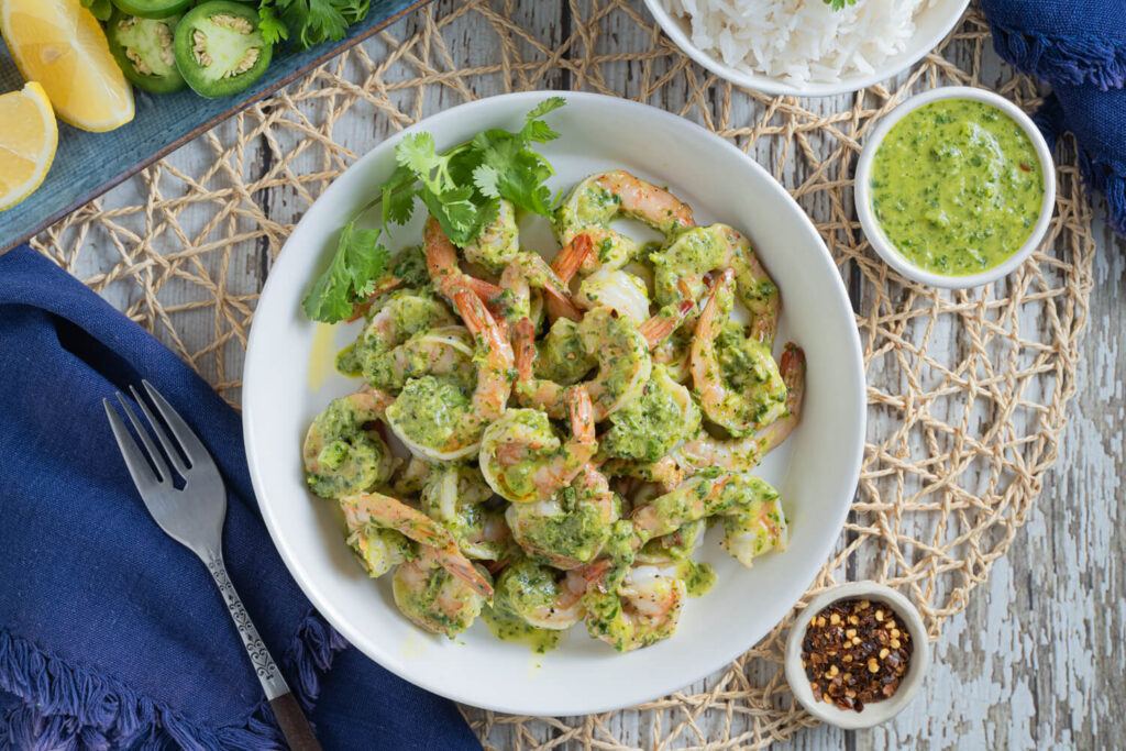 Overhead image of cooked shrimp with a vibrant green chimichurri sauce