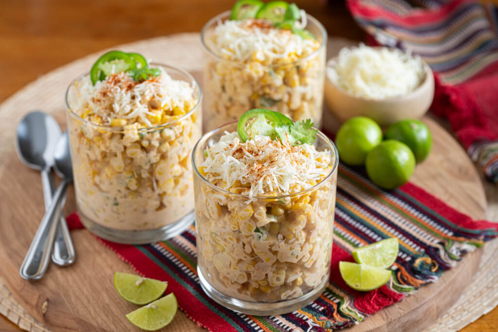 Three short glasses of Mexican street corn salad made with corn, cotija cheese, mayonnaise, and jalapenos for Cinco de Mayo.