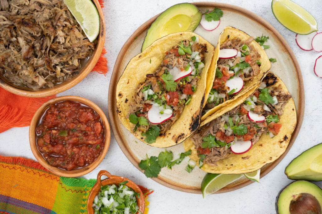 Overhead image of three pork carnitas tacos garnished with fresh veggies for a Cinco de Mayo celebration