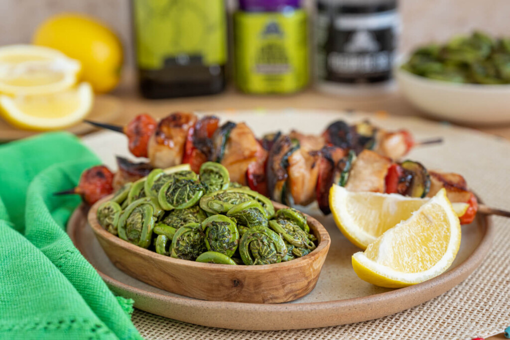 plate with kebabs, sauteed fiddleheads, and lemon wedges