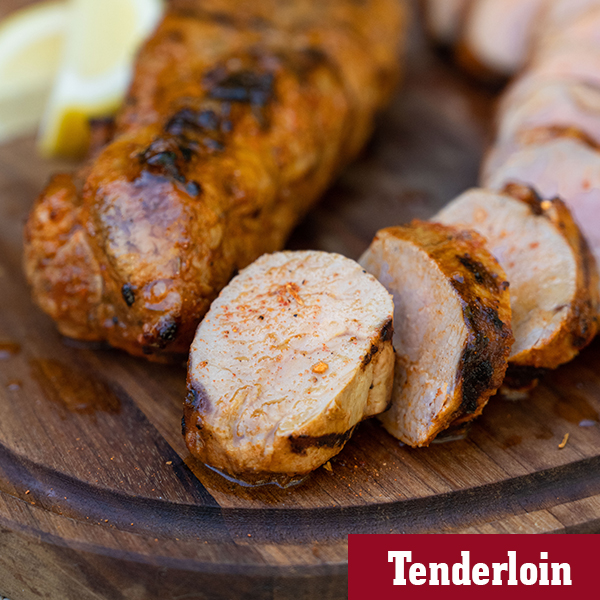 A wooden board with sliced and juicy spicy piri piri grilled pork tenderloin with lemon slices as garnish.