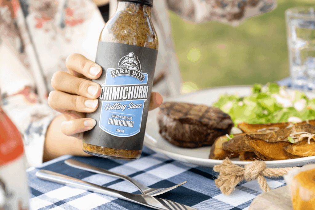 Hand holding Farm Boy Chimichurri Grilling Sauce at a summer BBQ