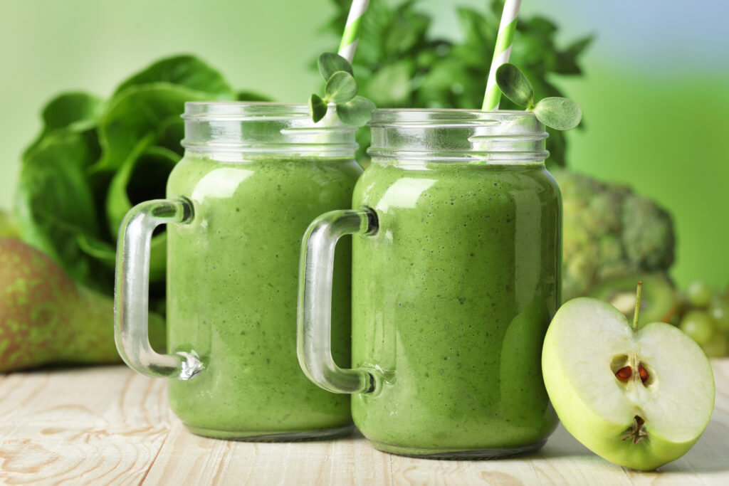 Mason jars of fresh green smoothie and ingredients on wooden table, closeup
