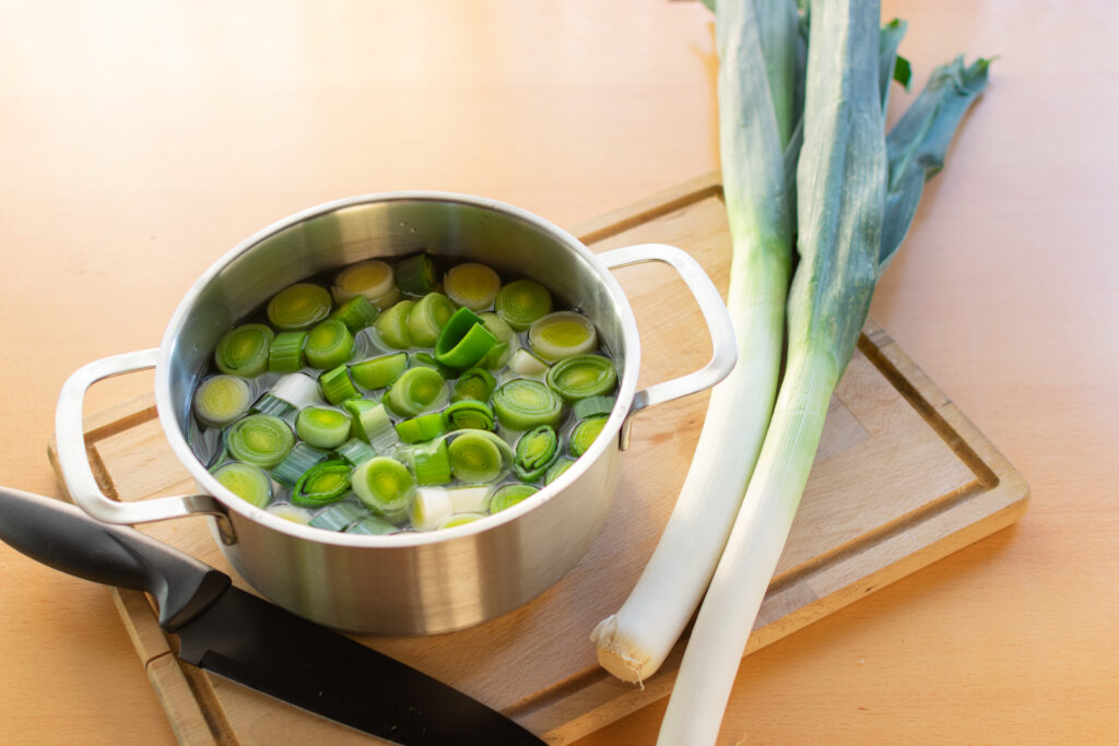 Whole Leek and Chopped Soaked Leeks on a cutting board with knife.