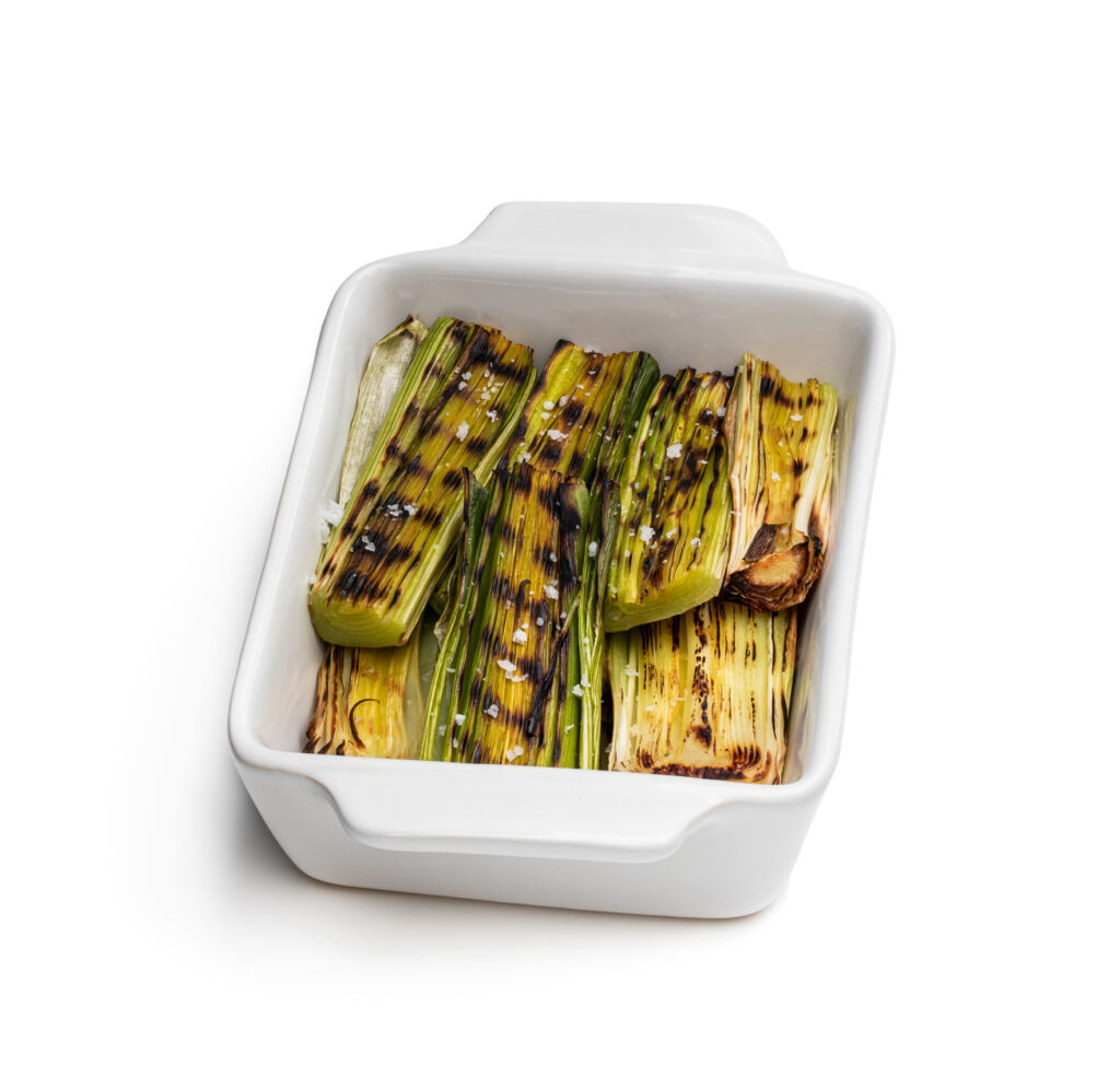 Grilled baby leeks in clay bowl isolated on white