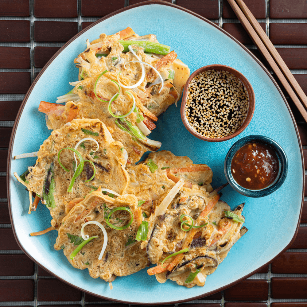 Overhead image of four vegetable pancakes on a blue plate with two small bowls of dipping sauces