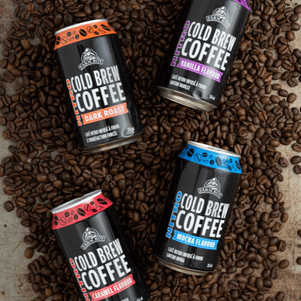 Overhead image of four different cans of Farm Boy Nitro Cold Brew Coffee lying on coffee beans.
