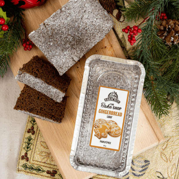 Ovehead shot of Farm Boy Gingerbread Loaf Cake in package and a loaf sliced as a holiday gift on a wooden cutting board with seasonal decor.