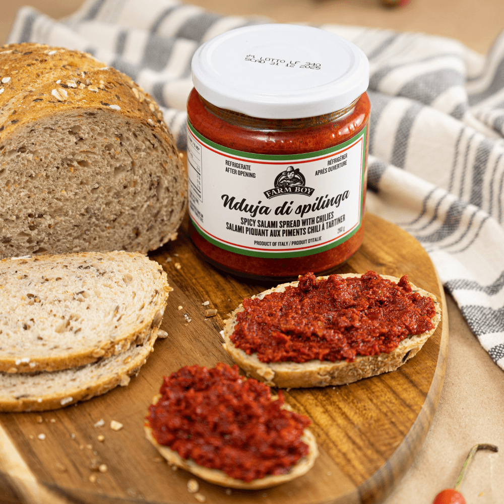Wooden cutting board with sliced multigrain boule. Two slices are covered in farm Boy Nduja di Spilinga