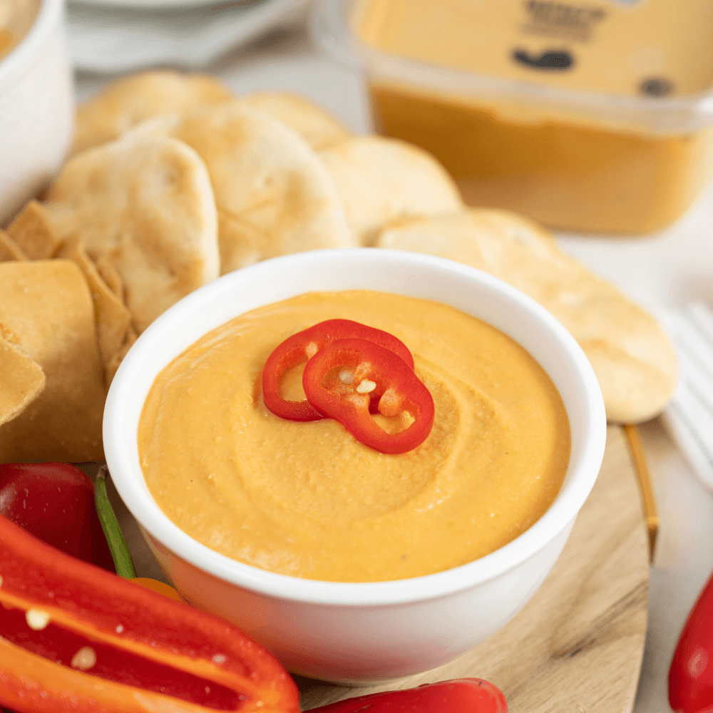 White bowl of spicy hummus garnished with fresh chili pepper rings