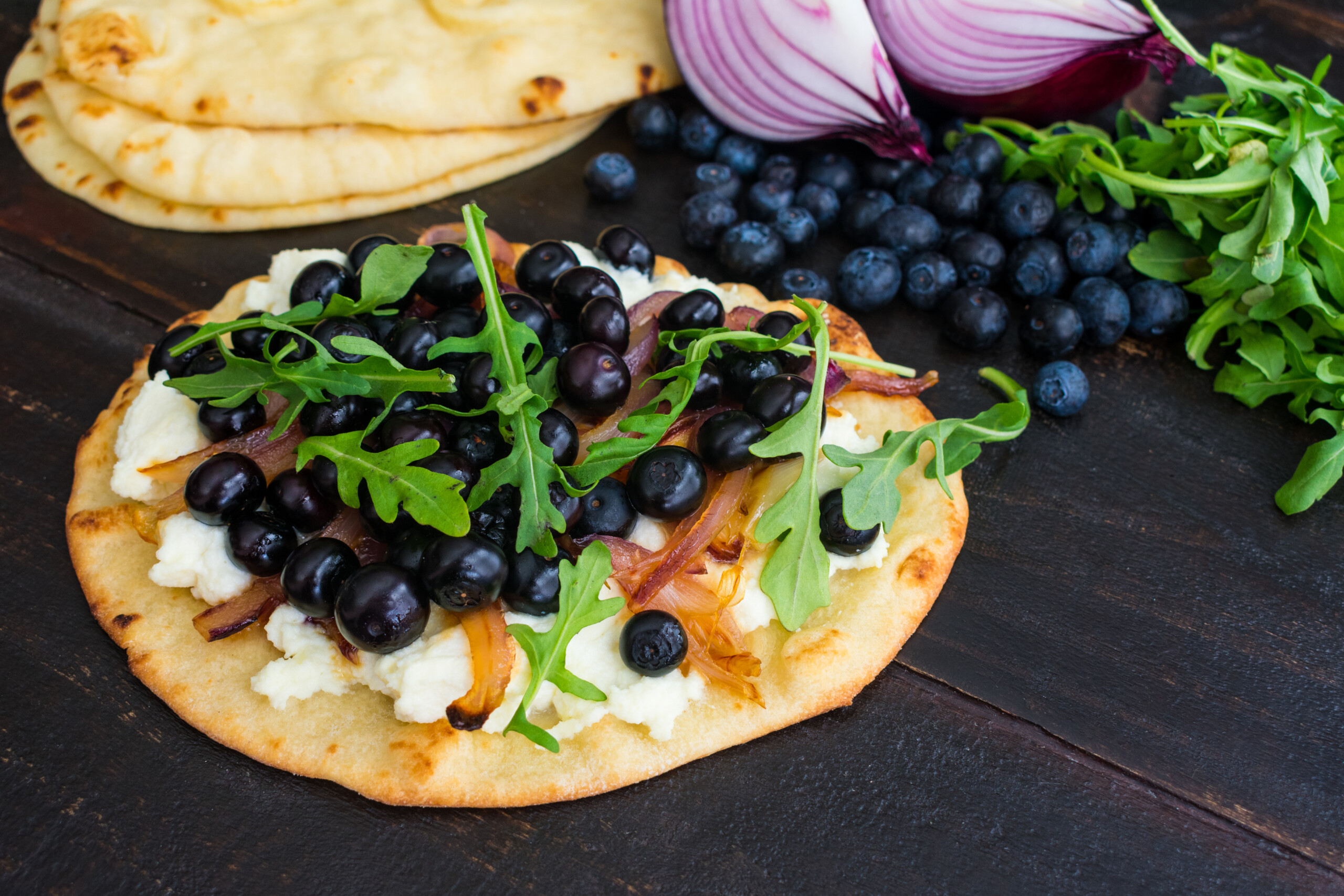 Naan pizza with goat cheese, caramelized onions, blueberries, and arugula.