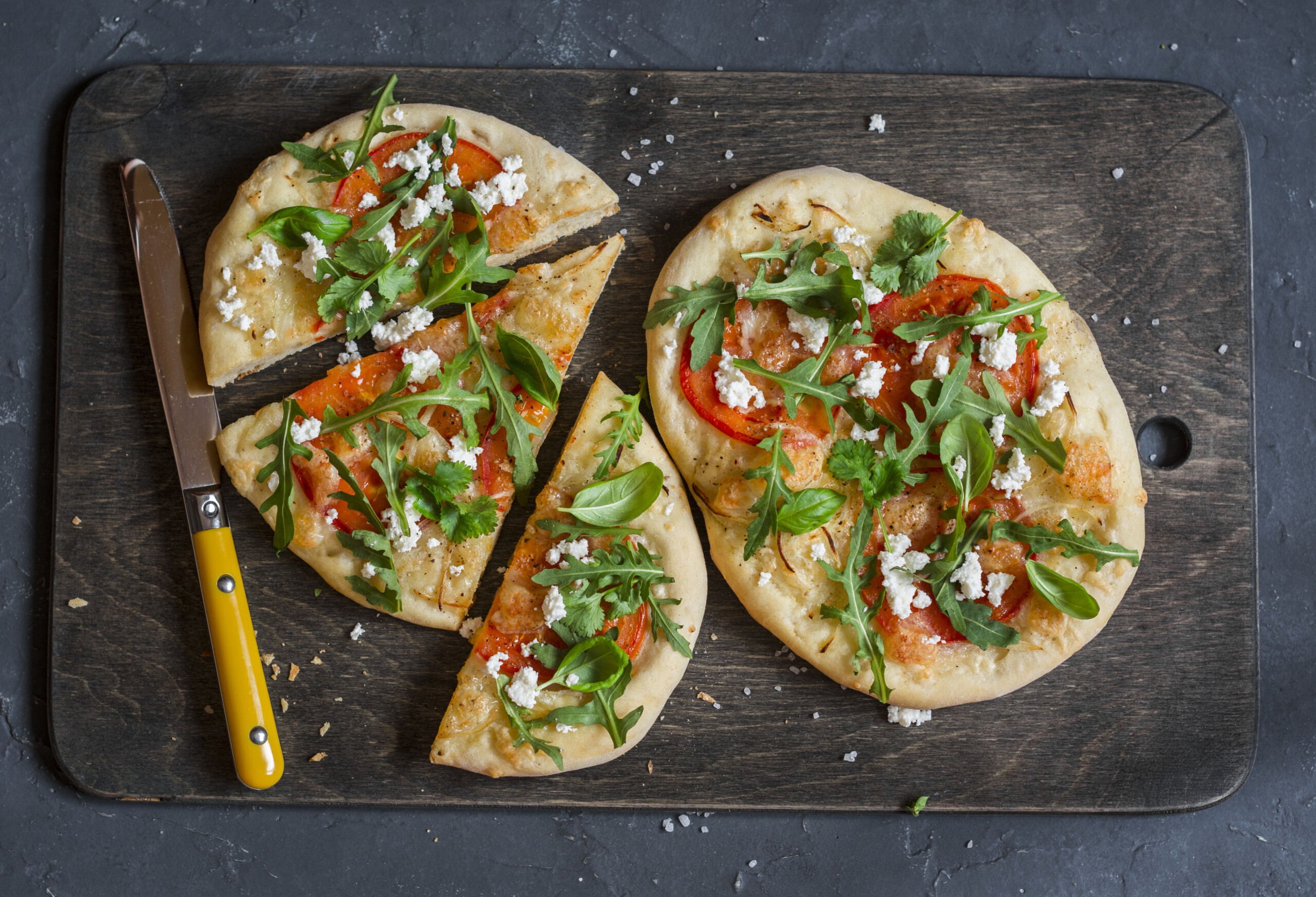 Naan pizza with goat cheese, sliced tomatoes, and arugula.