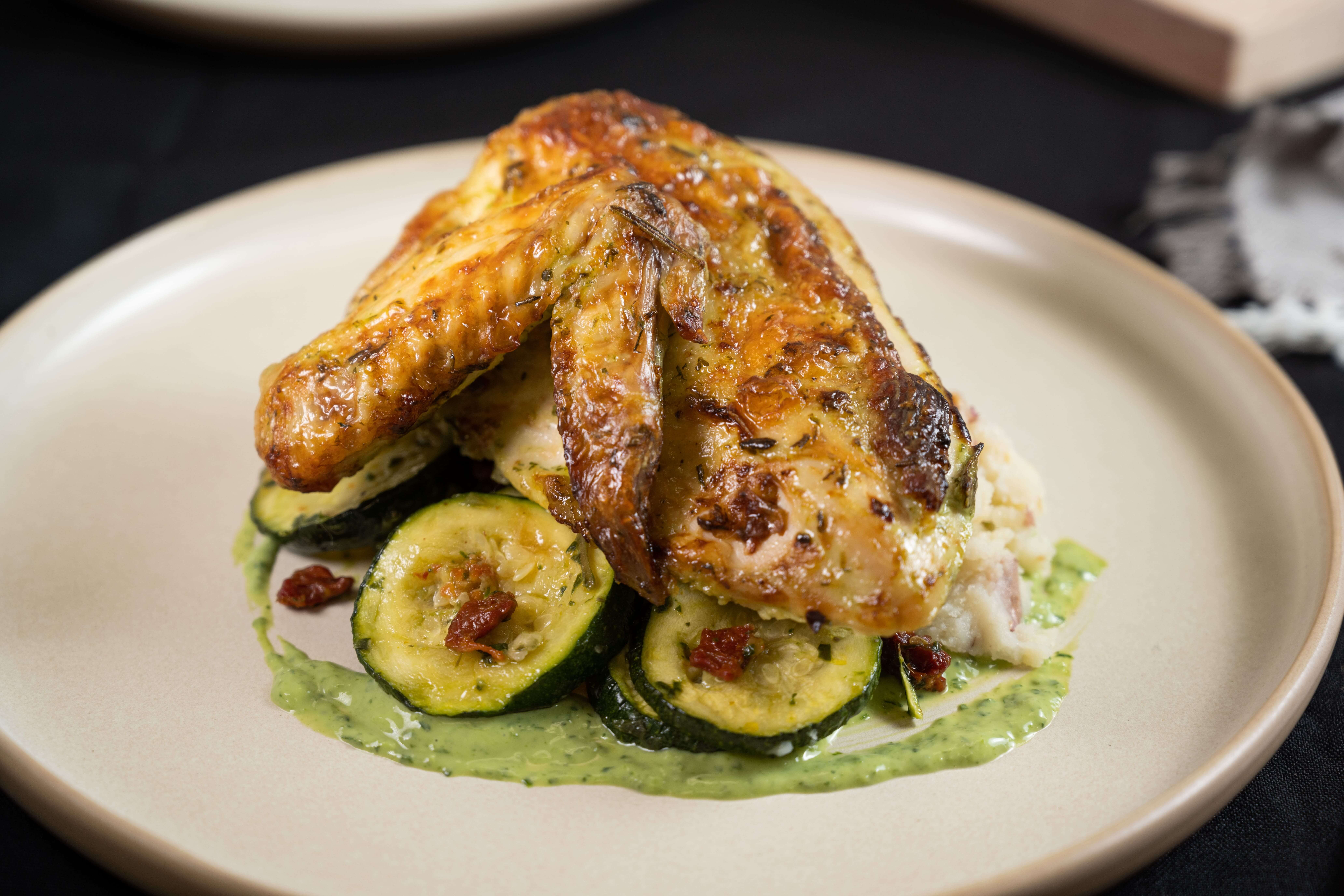 The image is a is a perfectly roasted, Green Goddess Chicken Supreme with a bright, zingy sauce and a side of Smokey Red Potatoes and herbaceous Courgette Provençale.