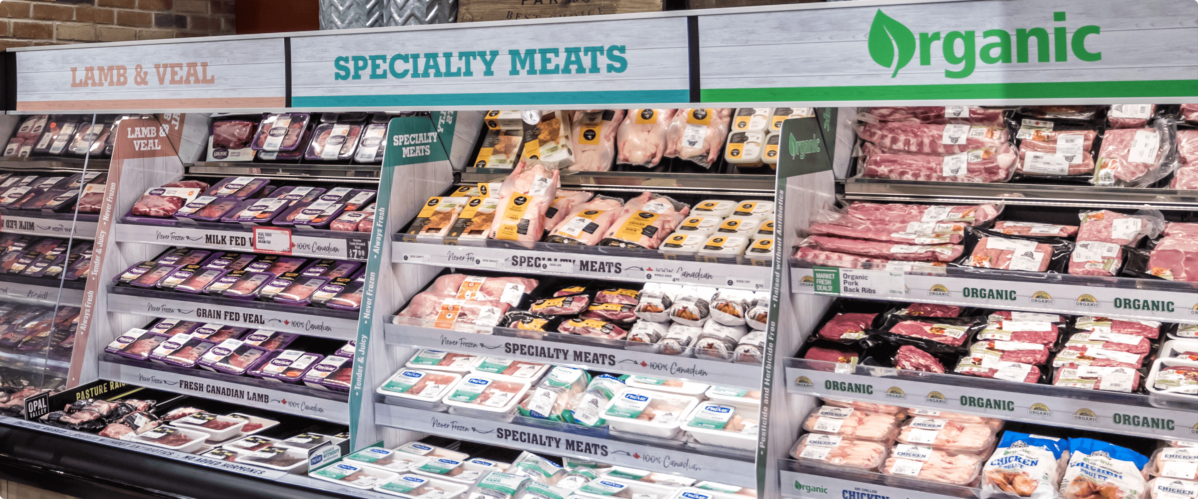 Packaged Meat Display A well-lit section of a Farm Boy store meat department with a variety of fresh meats on display in refrigerated cases. Signs above the cases advertise organic and specialty meats, including lamb, veal, and grain-fed veal.