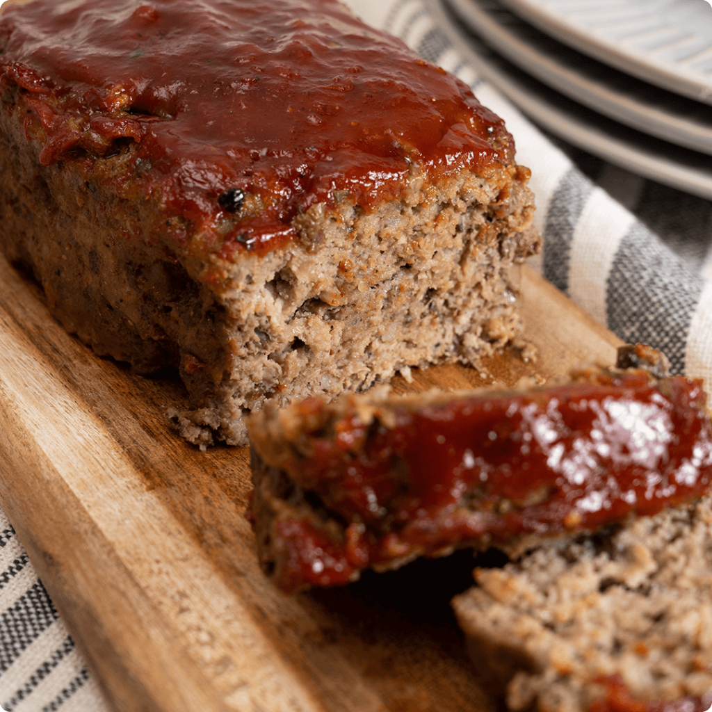 The image shows a ready-to-cook meatloaf available at Farm Boy. It appears to be a traditional meatloaf topped with a ketchup or barbecue sauce glaze, sliced and ready to serve.