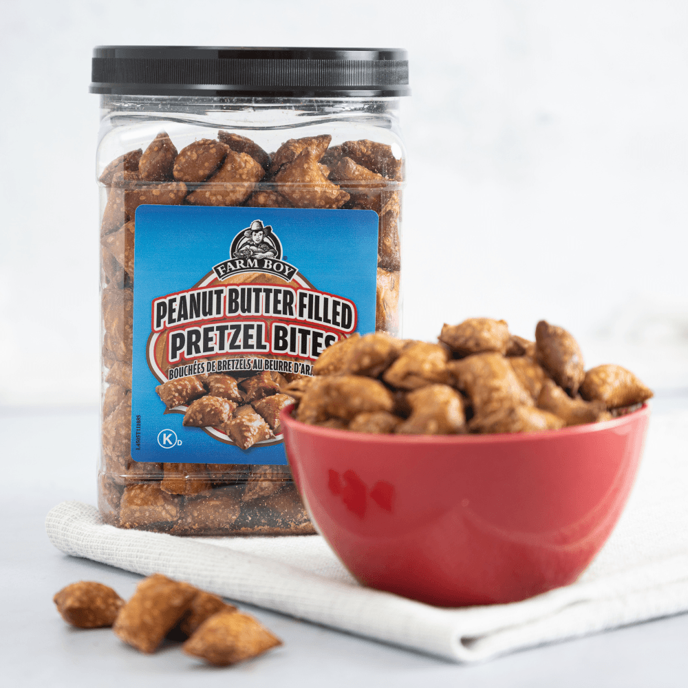 Tub of Farm Boy Peanut Butter Pretzel Bites with small red bowl in foreground filled with pretzel bites