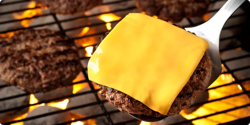 A slice of cheese on a griller burger patty placed on a spatula. 