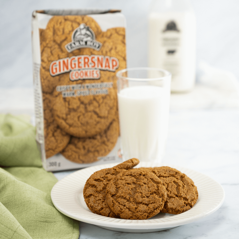 Plate of Farm Boy Gingersnap Cookies in front of glass of milk with bag of cookies in background.