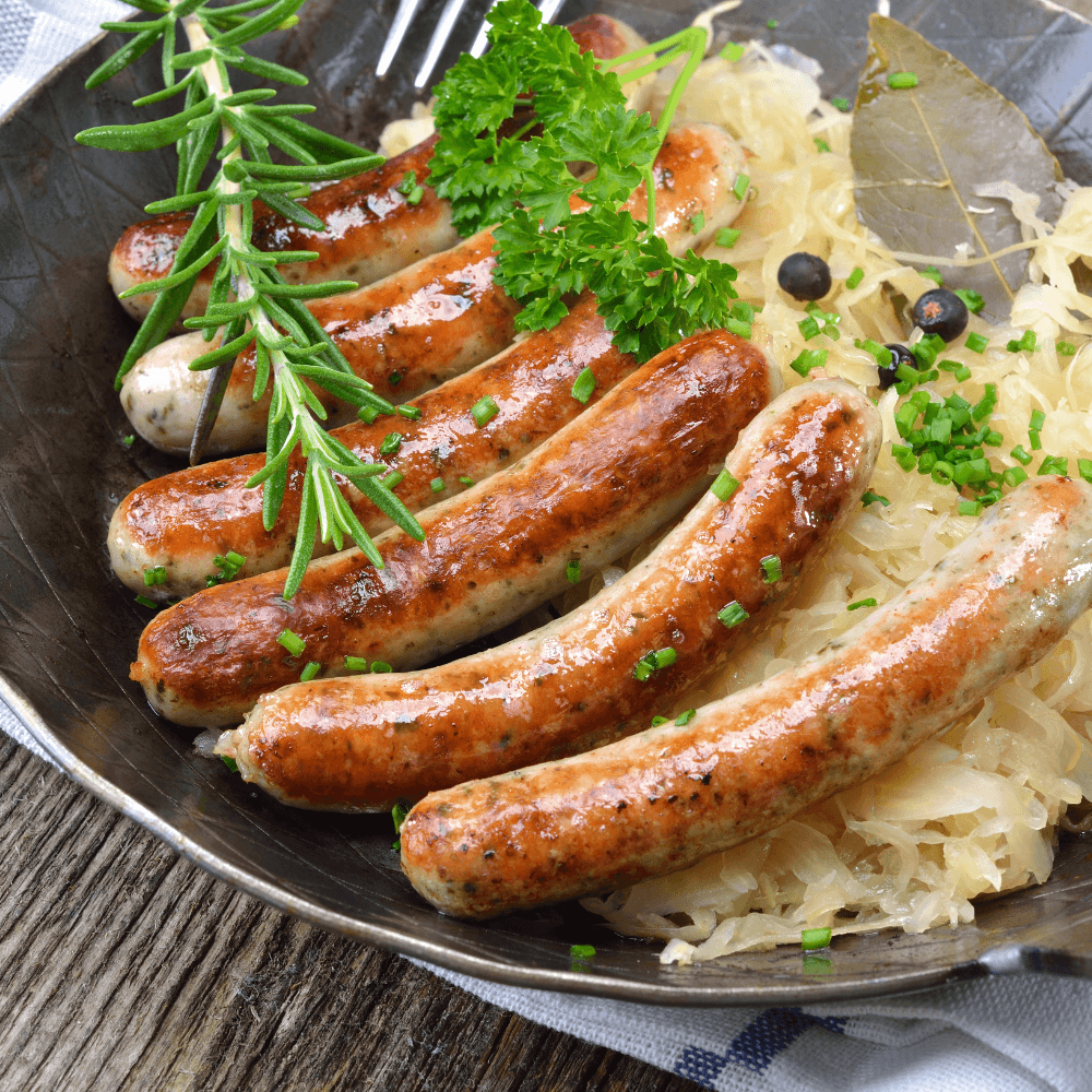 Stock image of six Oktoberfest sausages on a plate with sauerkraut and sprigs of fresh rosemary.