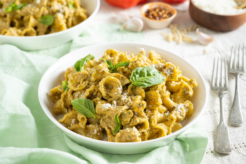 Pasta with Pesto Alla Trapanese garnished with parmesan cheese and fresh basil leaves in a white bowl next to a pale green napkin.