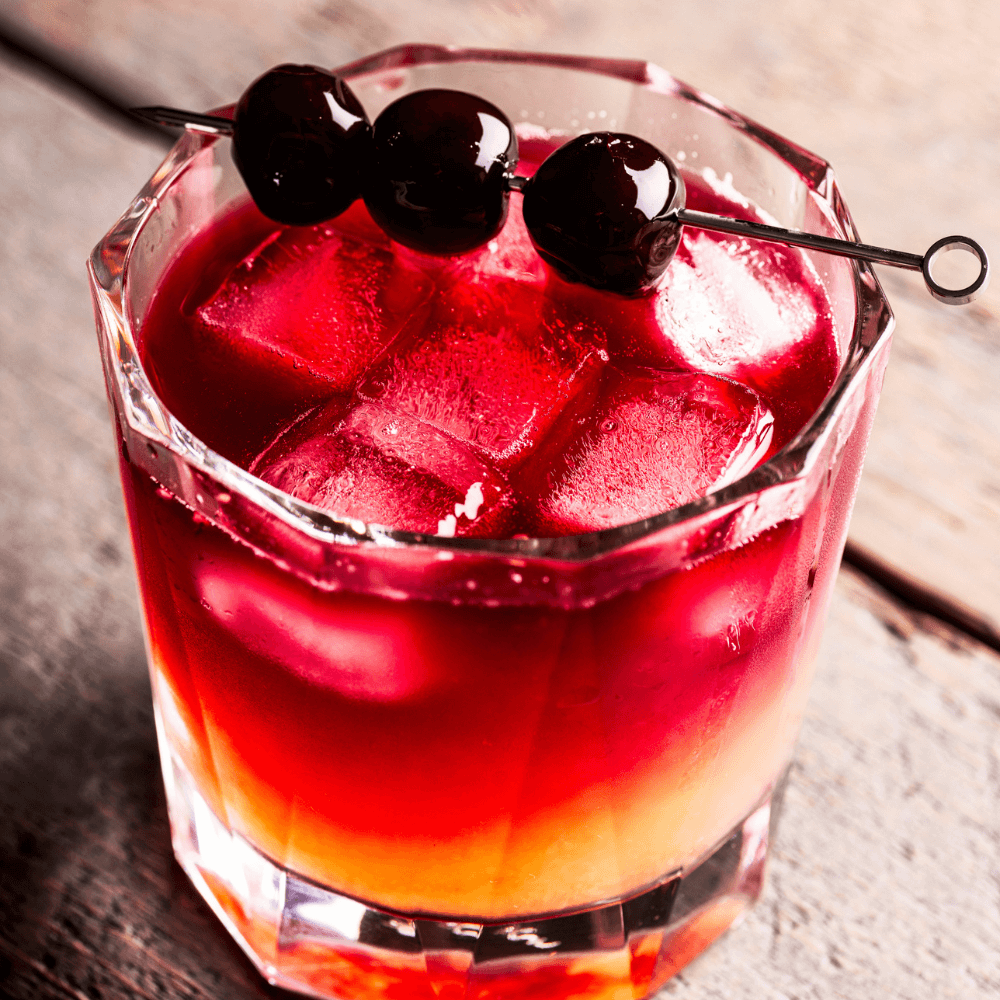 Whiskey sour in glass tumbler with cherry juice and garnish of dark cherries