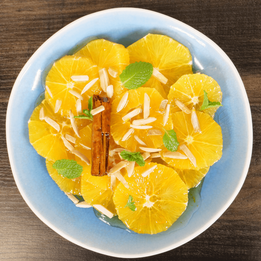 Blue plate with honey cinnamon oranges garnished with almond slivers, mint leaves, and cinnamon stick.