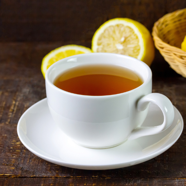 Cup of hot tea in white ceramic cup and fresh lemon on rustic wooden table.