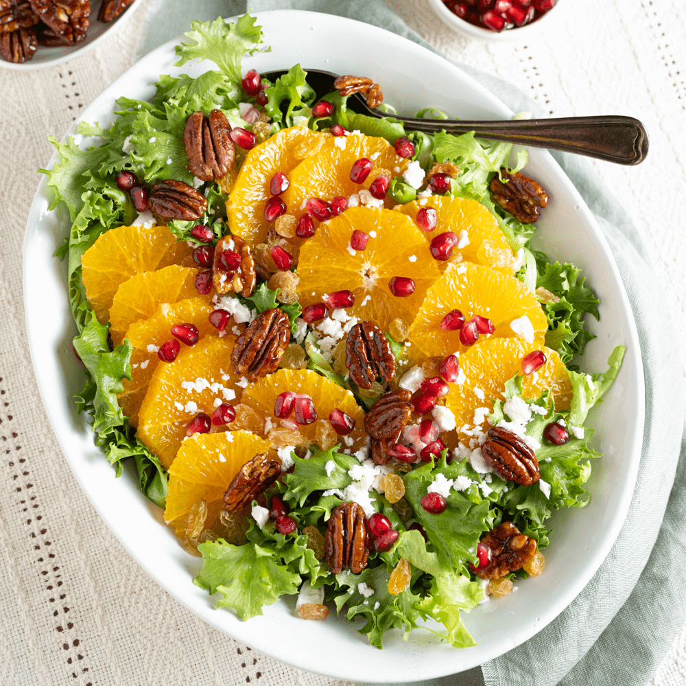 Overhead image of Winter Orange Salad on a serving platter, garnished with pomegranate seeds, cheese, and candied pecans.