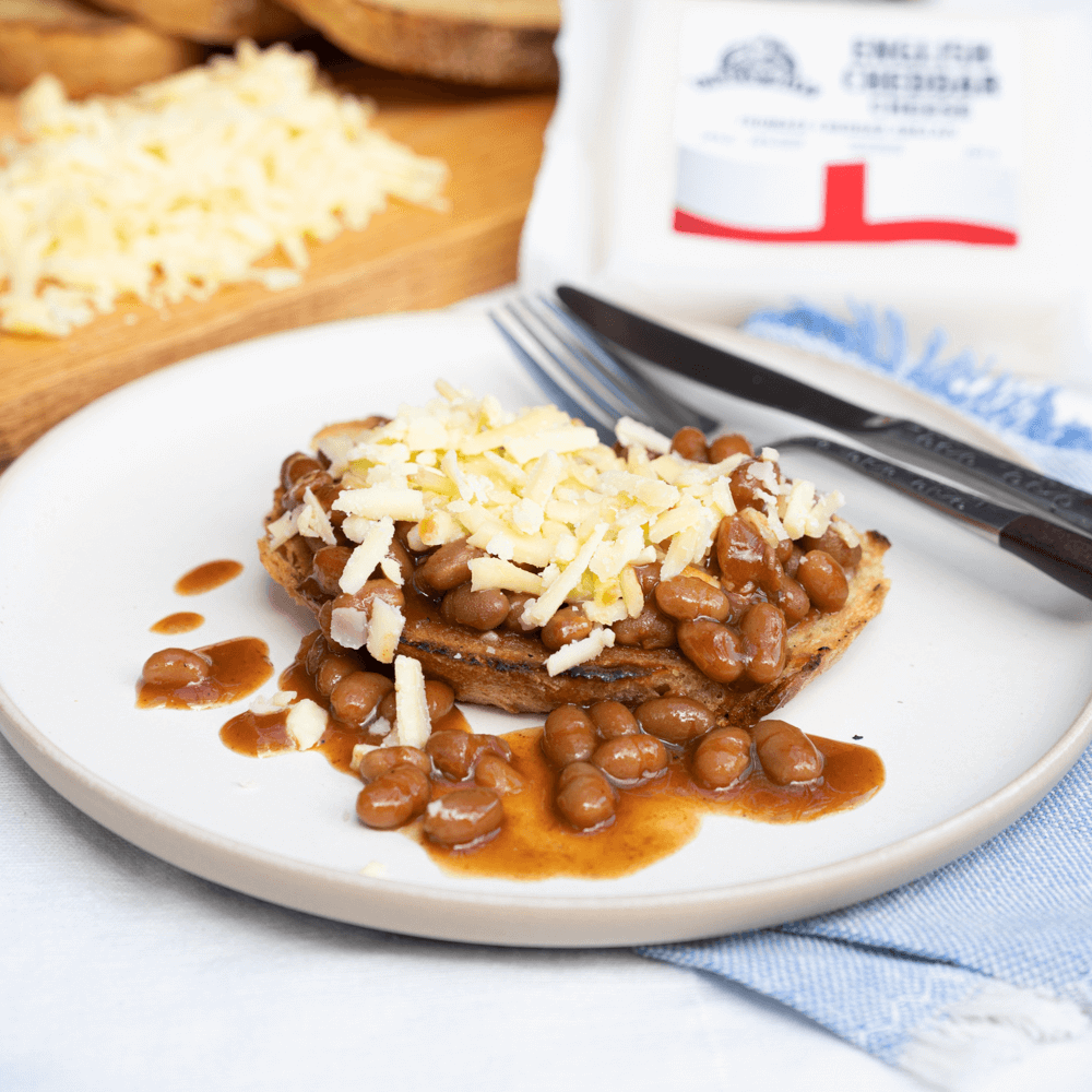 White plate with slice of bread covered in baked beans and shredded cheese.