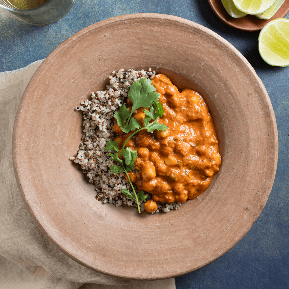 Overhead image of wooden bowl with butter chickpeas, mixed quinoa, and fresh cilantro.