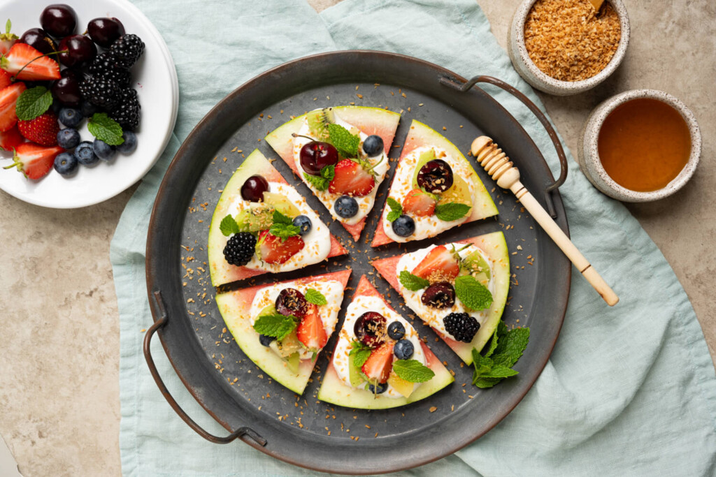 Overhead image of watermelon pizza with yogurt, honey, and mixed berries on cast iron serving tray