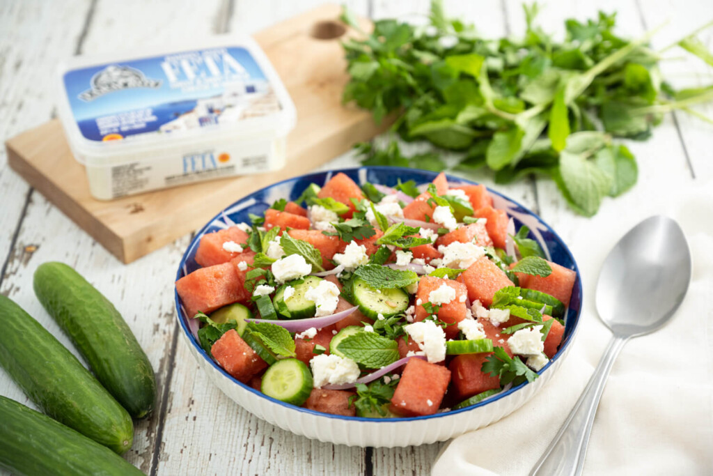 Plate of watermelon cucumber and feta salad on white wooden picnic table