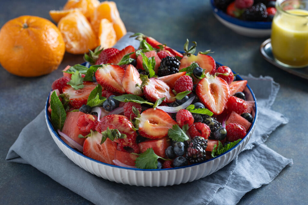 Bowl of mixed berry and watermelon salad with tangerines in background