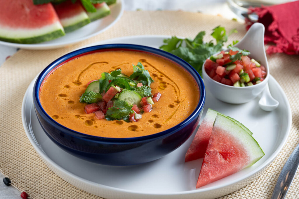 Bowl of watermelon tomato gazpacho with wedge of watermelon on plate