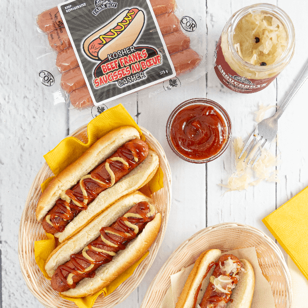 Overhead image of hot dogs dressed with ketchup and mustard next o package of Farm Boy Kosher Beef Franks