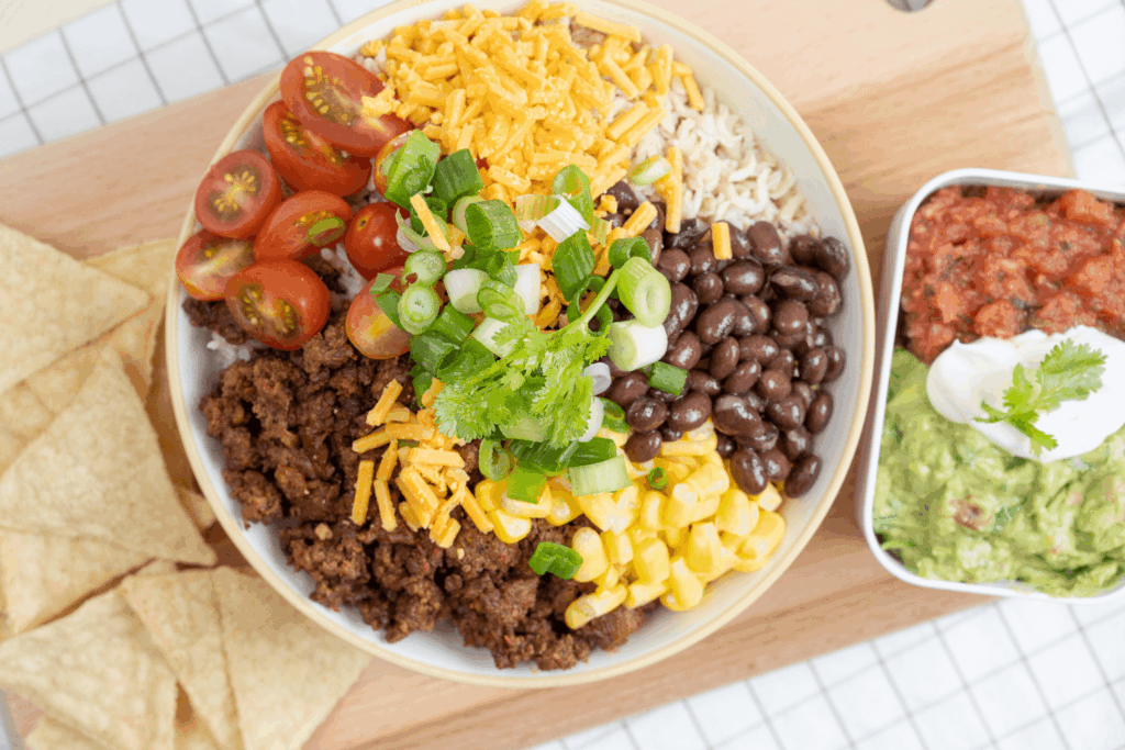 Overhead image of a ground beef taco bowl with black beans, corn, tomatoes, shredded cheese, and green onions