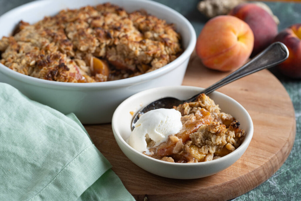 Dish of peach crumble with bowl of peach crumble topped with scoop of vanilla ice cream