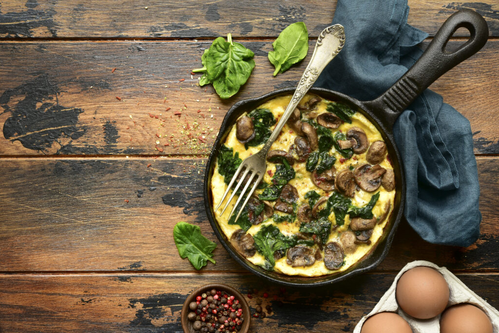 Omelette with mushrooms and spinach in a cast iron pan on a dark rustic wooden background.Top view with copy space.