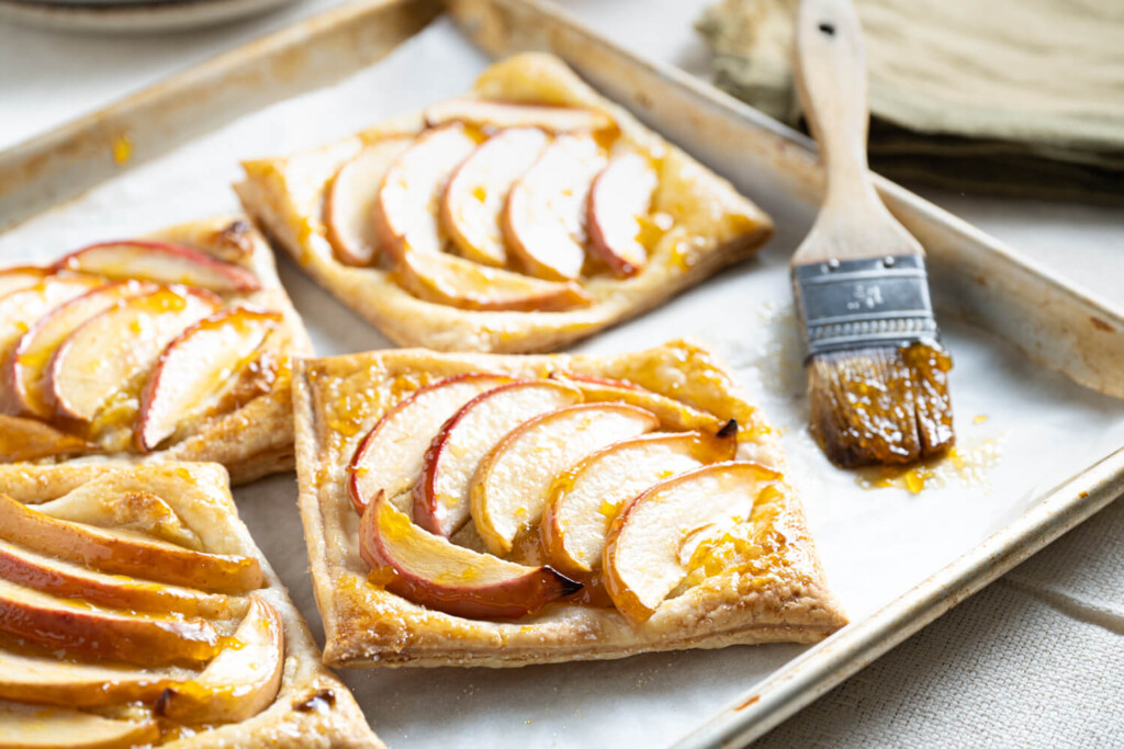 Close up image of apple tarts on baking sheet with pastry brush